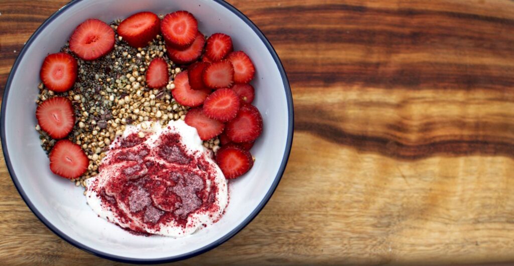 Queen Garnet homemade oat-free muesli + yoghurt in a bowl on a table spread, with topping and a wooden spoon alongside