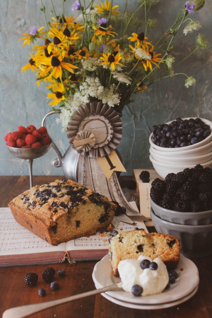 Gluten Free Banana and Plum bread sitting on a coffee table, with plums & berries in a bowl alongside