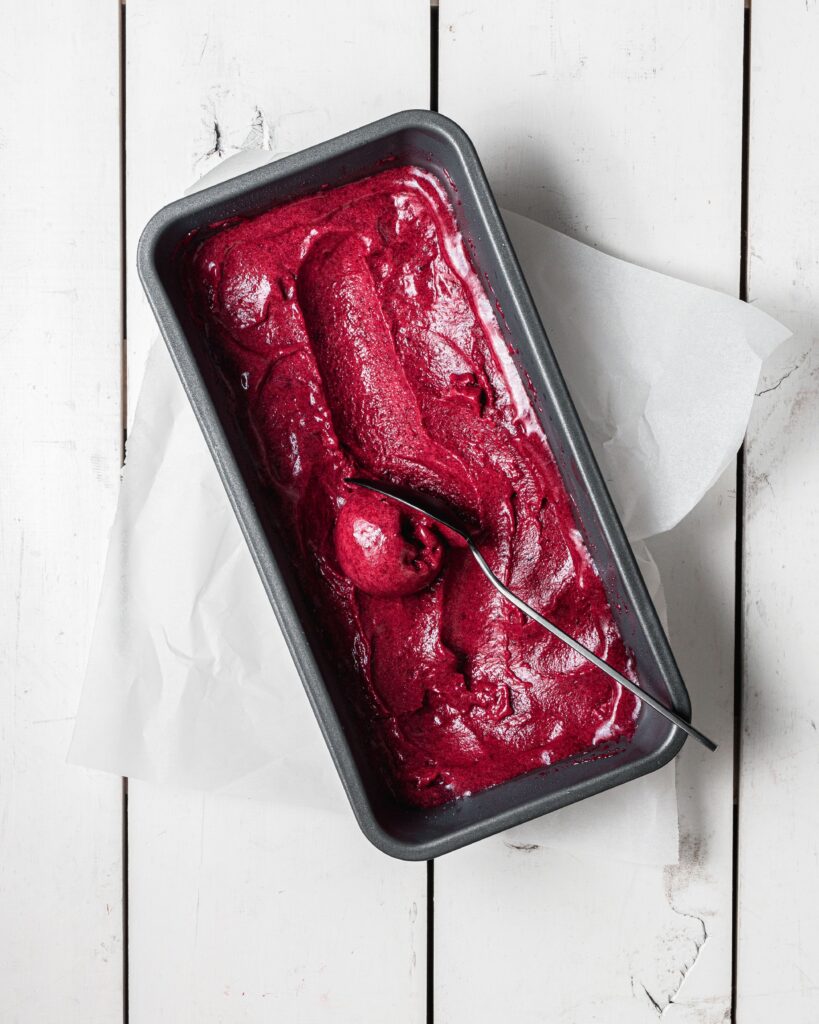 A pan of Queen Garnet plum sorbet, with a spoon taking out a scoop