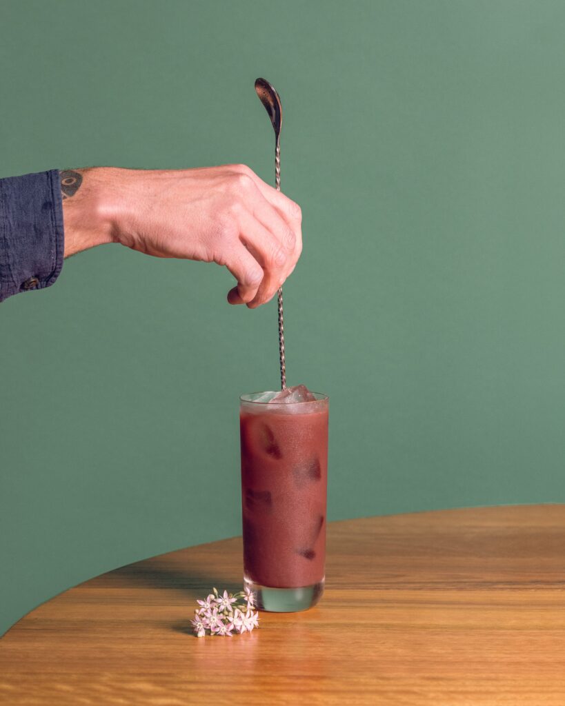 Queen Garnet Queen Mary cocktail being stirred on a wooden table